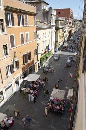 A bustling street with outdoor cafes, pedestrians, and parked cars. - Borgo Pio 91 (Rome)