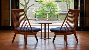 Two wooden chairs with blue cushions, a small round table, and a view of a courtyard with trees and a building in the background. - Hakone Yutowa (Hakone)