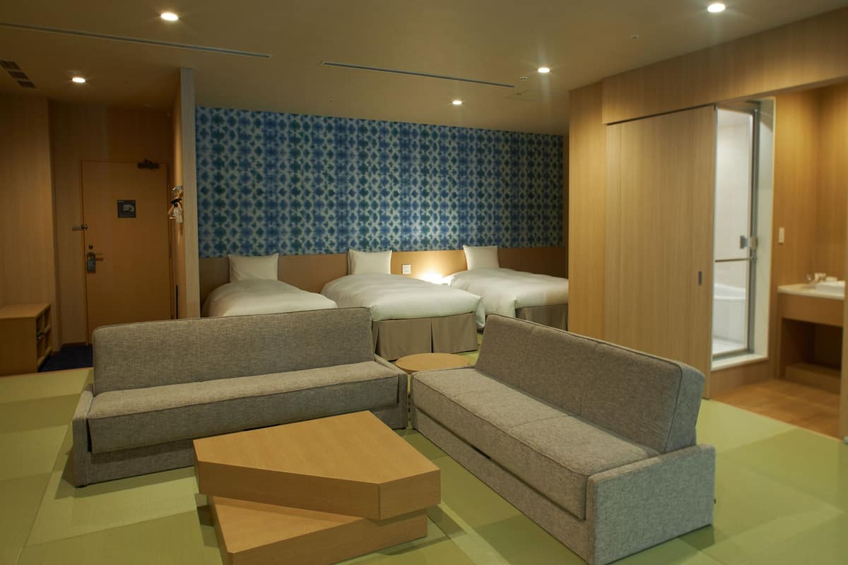 A hotel room with a sofa set, a small wooden table, and a bed with a patterned headboard.