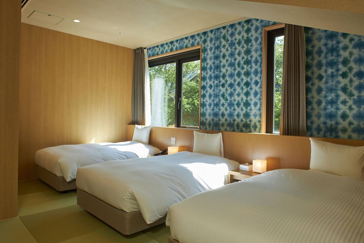 A hotel room with two beds, a large window, and a view of trees.