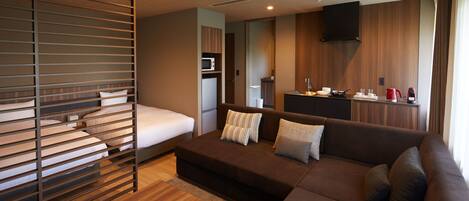Una habitación de hotel moderna con una cama, un sofá, una mesa de madera, una kitchenette y un televisor montado en la pared.