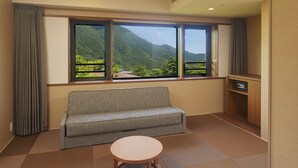 A hotel room with a sofa, a small round table, a desk, and a window offering a view of a mountainous landscape. - Hakone Yutowa (Hakone)