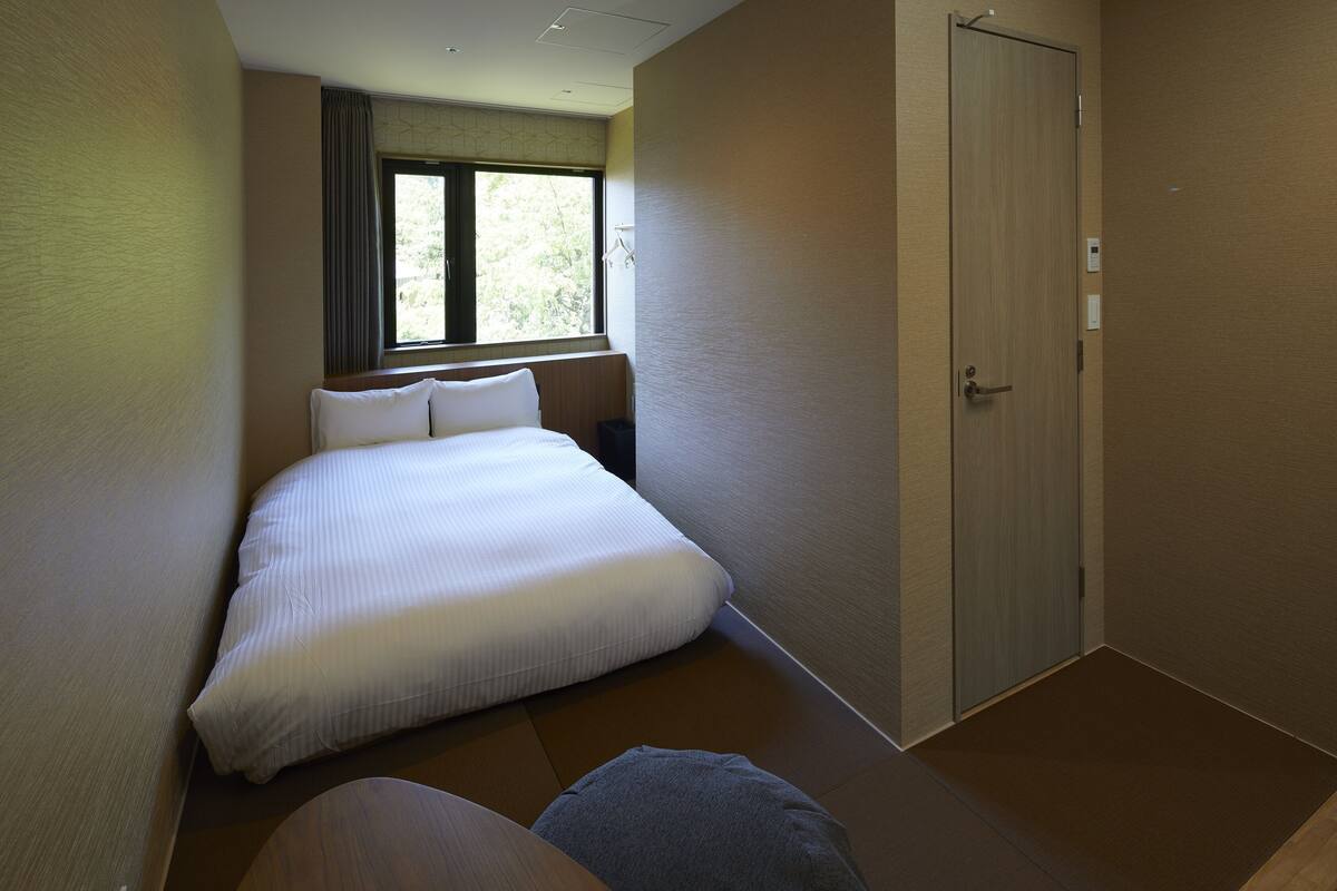 A hotel room with a large bed, a bedside table, a window with curtains, and a door.