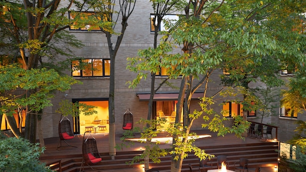 A modern outdoor deck with seating and a fire pit, surrounded by trees and a building with large windows. - Hakone Yutowa (Hakone)