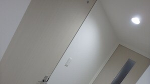 A narrow hallway with a door at the end, a light switch, and a small vent on the wall. - YADO at Tennouji Namba ExTen (Osaka)
