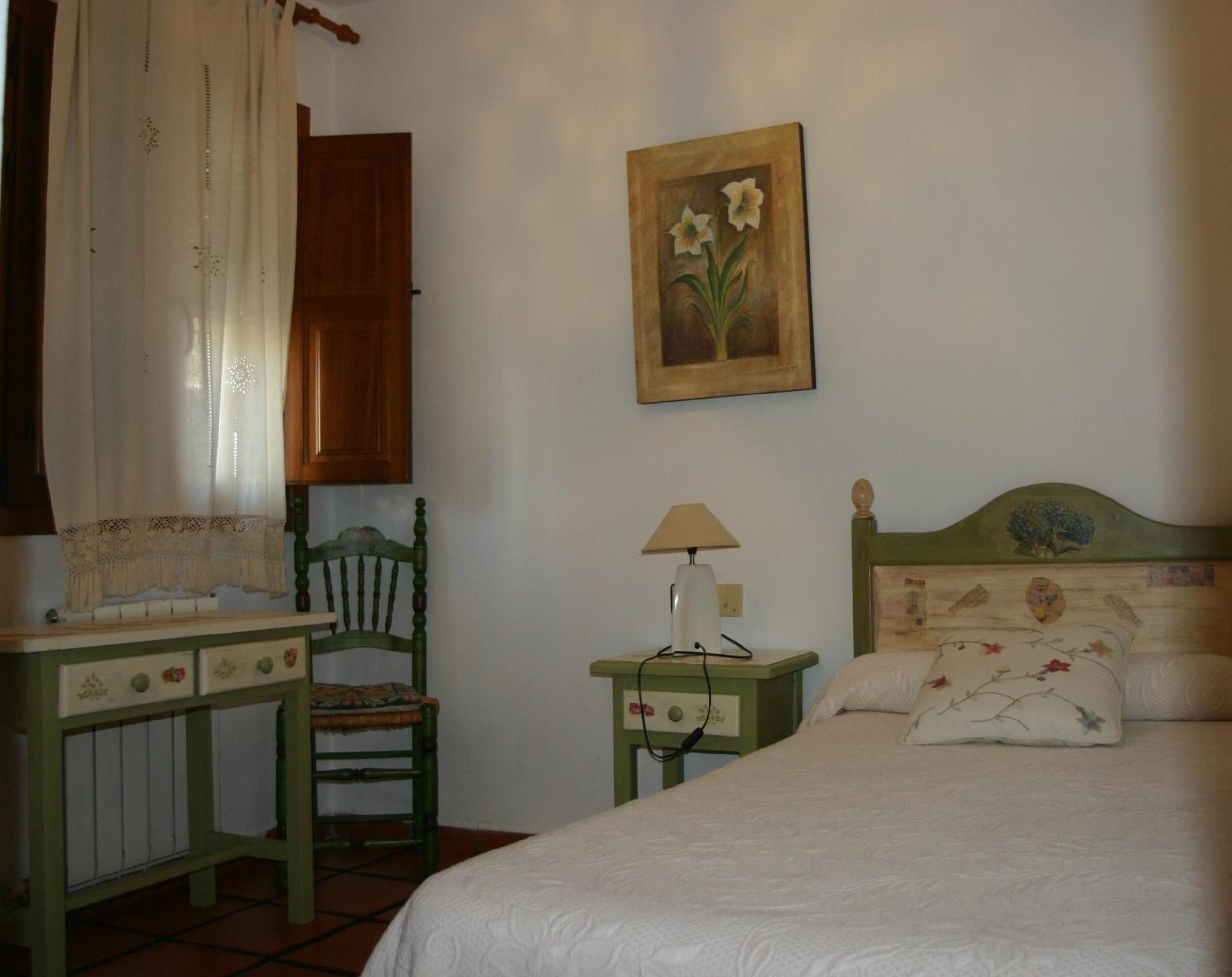 A bedroom with a bed, a chair, a nightstand, a lamp, and a painting on the wall.
