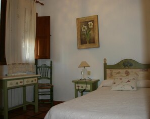 A bedroom with a bed, a chair, a nightstand, a lamp, and a painting on the wall. - Hostal Las Terrazas de la Alpujarra (Bubion)