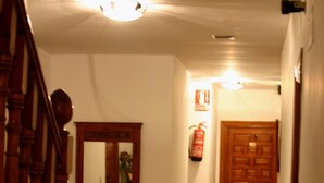 A hallway with a wooden staircase, a fire extinguisher, and a door at the end. - Hostal Las Terrazas de la Alpujarra (Bubion)