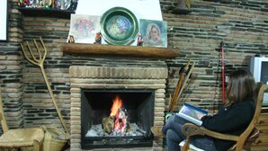 A person sitting by a fireplace with a book, surrounded by rustic decor and a brick wall. - Hostal Las Terrazas de la Alpujarra (Bubion)