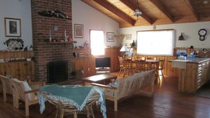 A spacious living area with a fireplace, wooden furniture, a television, and a kitchen area with a sink and counter. - The Beach Break (SMITHS BEACH)