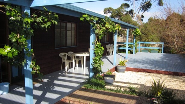 A wooden house with a blue porch, white plastic chairs, and a small table. - The Beach Break (SMITHS BEACH)