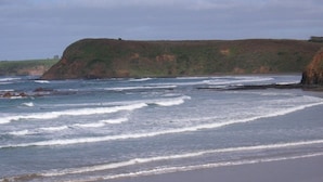 A beach with waves crashing onto the shore, a sandy beach, and a grassy cliff in the background. - The Beach Break (SMITHS BEACH)