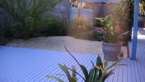 A wooden deck with a potted plant, gravel area, and a brick wall. - The Beach Break (SMITHS BEACH)