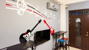 A room with a wall mural of musical notes and guitars, a flat-screen TV, a small table, a stool, and a door with a shoe design. - Seven Dwarfs (Puli)