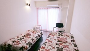 Quarto de hotel com duas camas, televisão, mesa pequena e janela com cortinas.