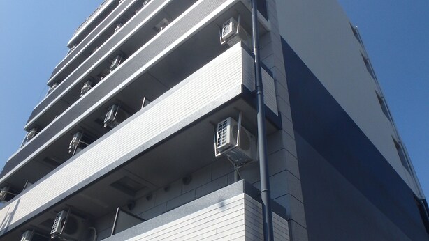 Um edifício de vários andares com design moderno, com unidades de ar condicionado em cada andar e uma escada de incêndio visível na fachada.