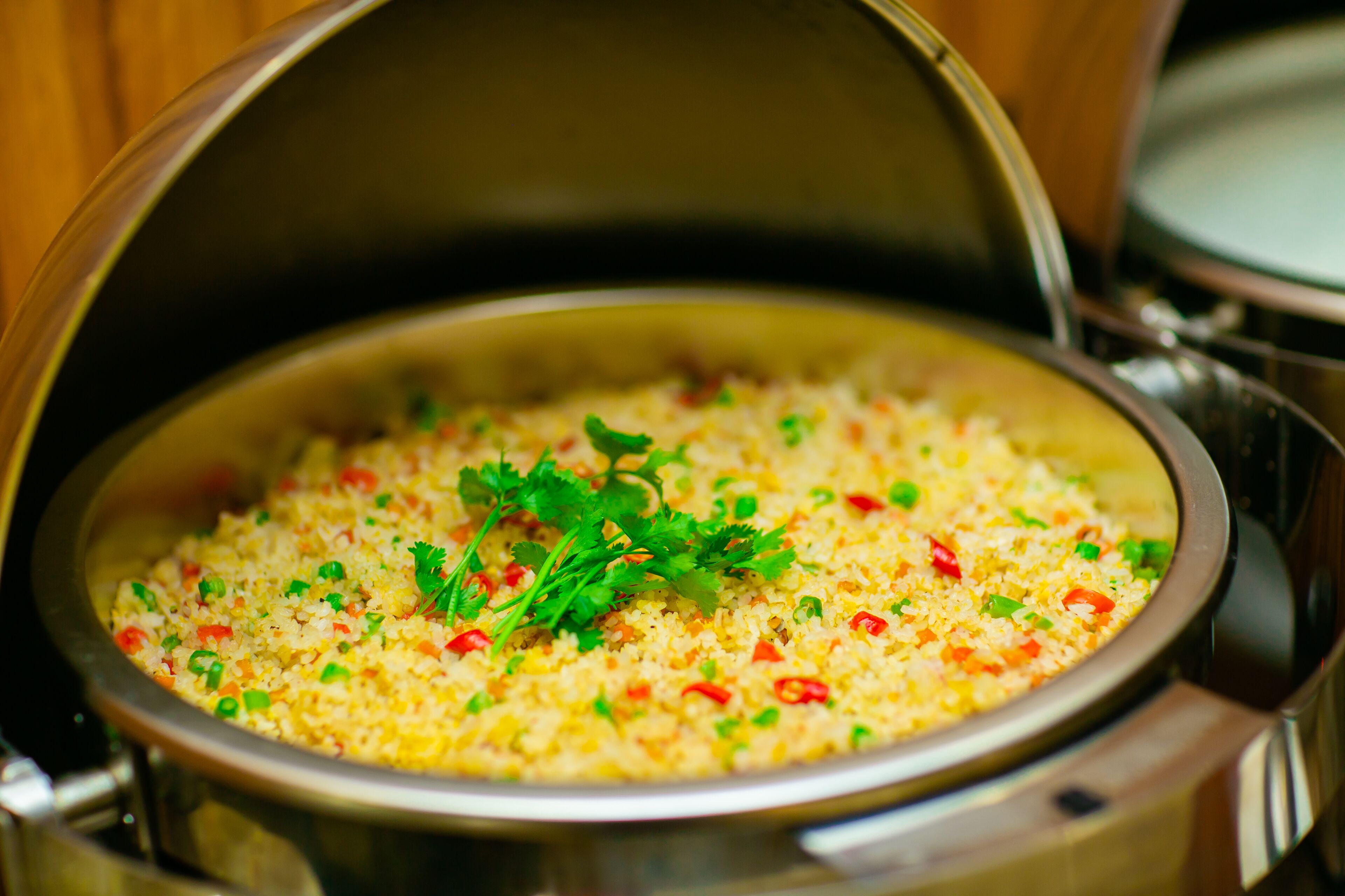 A close-up of a pot of fried rice garnished with green herbs and red peppers.