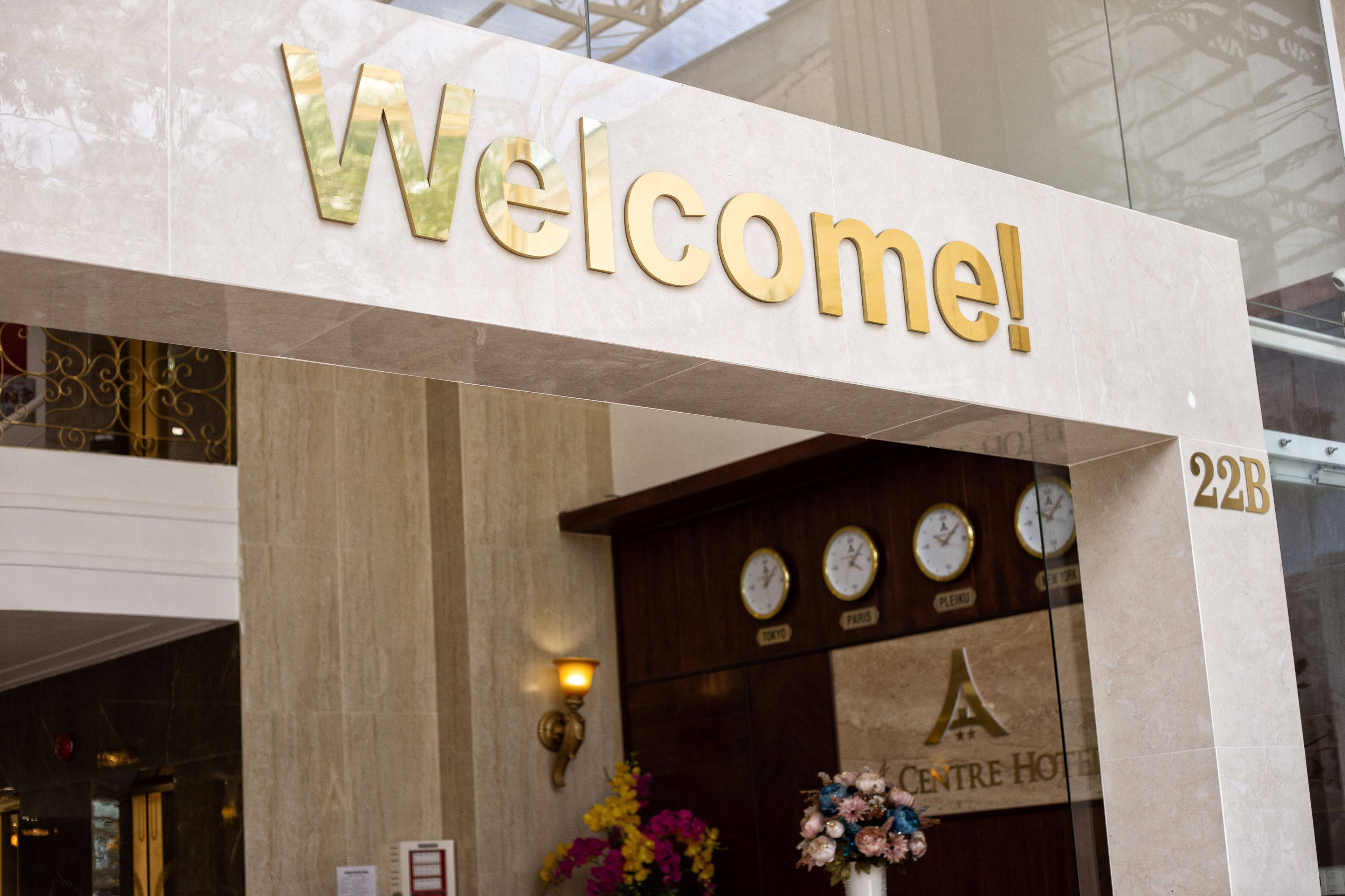 A hotel entrance with a 'Welcome!' sign, a clock display, and the number '22B'.