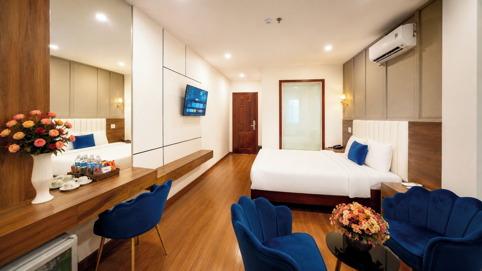 A hotel room with a bed, a desk with a vase of flowers, a TV, and a coffee station.
