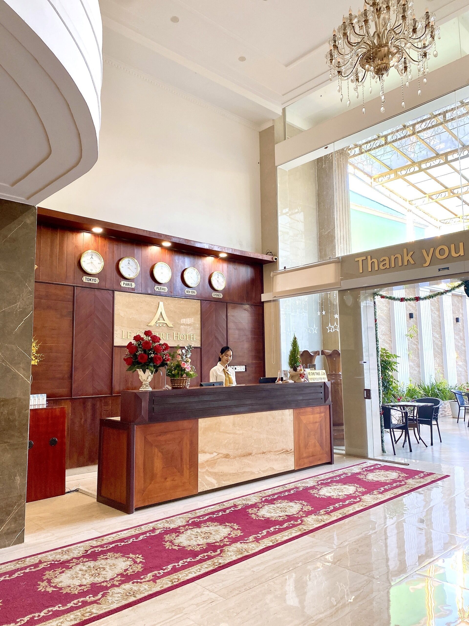 Zona de recepción de un hotel con un mostrador de madera, relojes mostrando la hora en diferentes ciudades y un cartel que dice 'Gracias' sobre el mostrador.