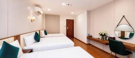 A hotel room with two beds, a wooden floor, a desk with a chair, a mirror, and a door.