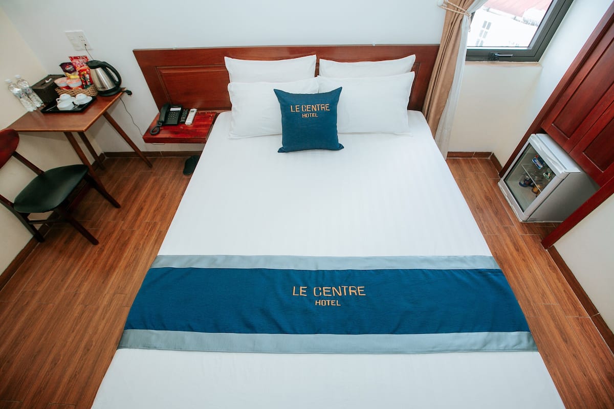 Una habitación de hotel con una cama, un escritorio con teléfono, una silla y un refrigerador pequeño.