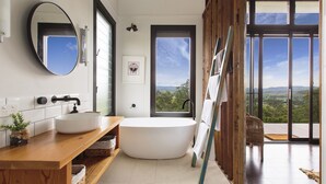 A modern bathroom with a freestanding bathtub, a large mirror, and a view of the outdoors through a large window. - “A Secret place to slow down” (Gloucester)