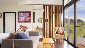 A modern living room with a grey sofa, a wooden coffee table, and a wicker chair. A large window offers a view of the outdoors. - “A Secret place to slow down” (Gloucester)