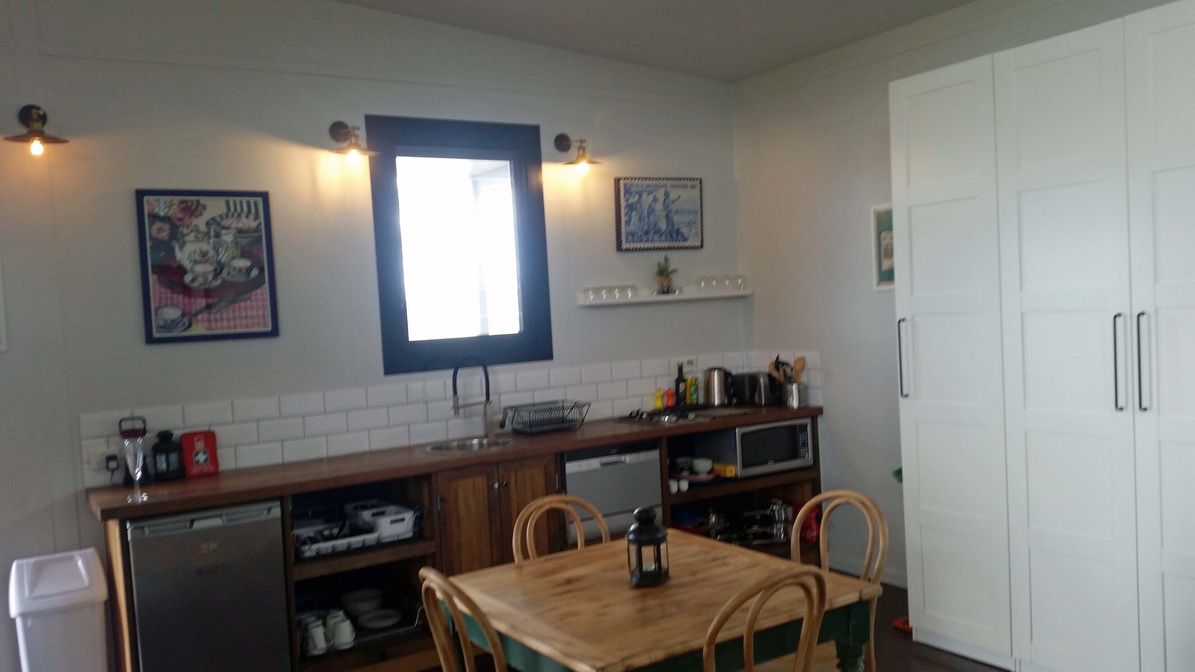 Une cuisine compacte dotée d’un plan de travail en bois, d’un lave-vaisselle encastré, d’un four à micro-ondes et d’une table à manger avec des chaises. Des luminaires sont fixés au mur et une fenêtre se trouve au-dessus de l’évier.
