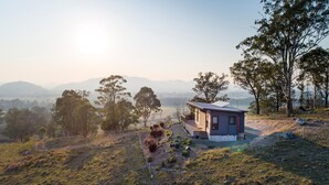 A small cabin with a wooden deck and a metal roof, surrounded by trees and hills. - “A Secret place to slow down” (Gloucester)
