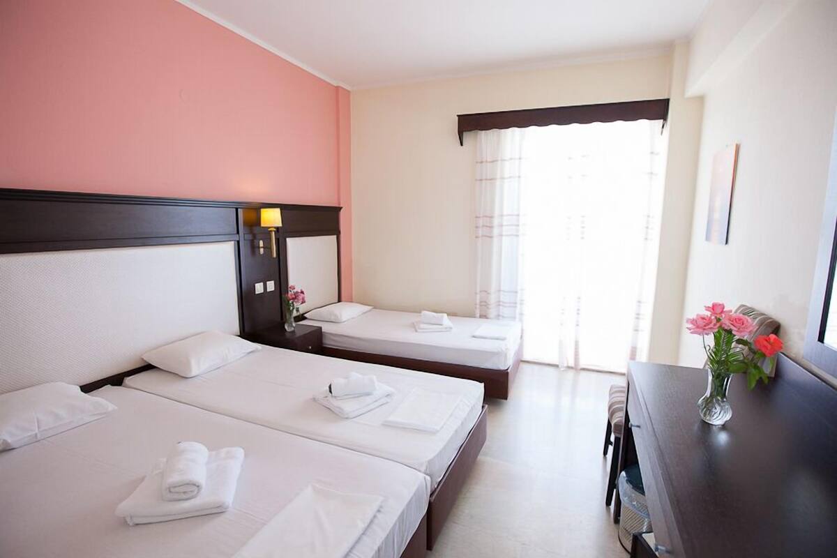 A hotel room with two beds, a desk, and a window with curtains.