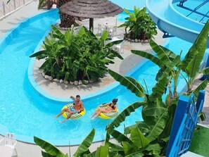 A swimming pool with two people on inflatable rings, surrounded by lush greenery and a thatched-roof structure. - Hotel Kanali (Preveza)