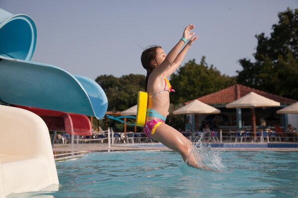 A child jumping into a pool with a water slide in the background. - Hotel Kanali (Preveza)
