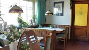 A dining area with wooden furniture, a window with curtains, and hanging lamps. - Hotel Restaurant Wulf (Ense)