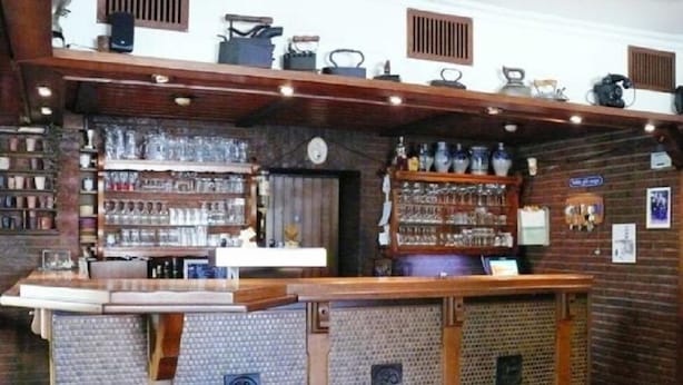 A bar area with shelves of glasses and bottles, a wooden counter, and a brick wall. - Hotel Restaurant Wulf (Ense)