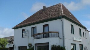 A two-story building with a tiled roof, a balcony with a black railing, and a sign indicating it is a hotel. - Hotel Restaurant Wulf (Ense)