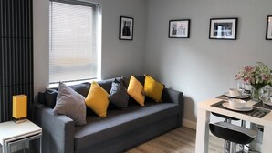 A modern living room with a grey sofa, yellow cushions, a dining table with chairs, and framed pictures on the wall. - City Central Townhouse by BHR Apartments (Belfast)