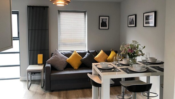 A modern living room with a sofa, a dining table, and a kitchen area. - City Central Townhouse by BHR Apartments (Belfast)