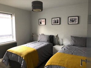 A bedroom with two beds, a window with blinds, and three framed pictures on the wall. - City Central Townhouse by BHR Apartments (Belfast)