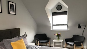 A bedroom with a bed, two chairs, a small table with a vase, a clock, and a window. - City Central Townhouse by BHR Apartments (Belfast)