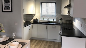 A modern kitchen with white cabinets, a black countertop, and a window with blinds. - City Central Townhouse by BHR Apartments (Belfast)