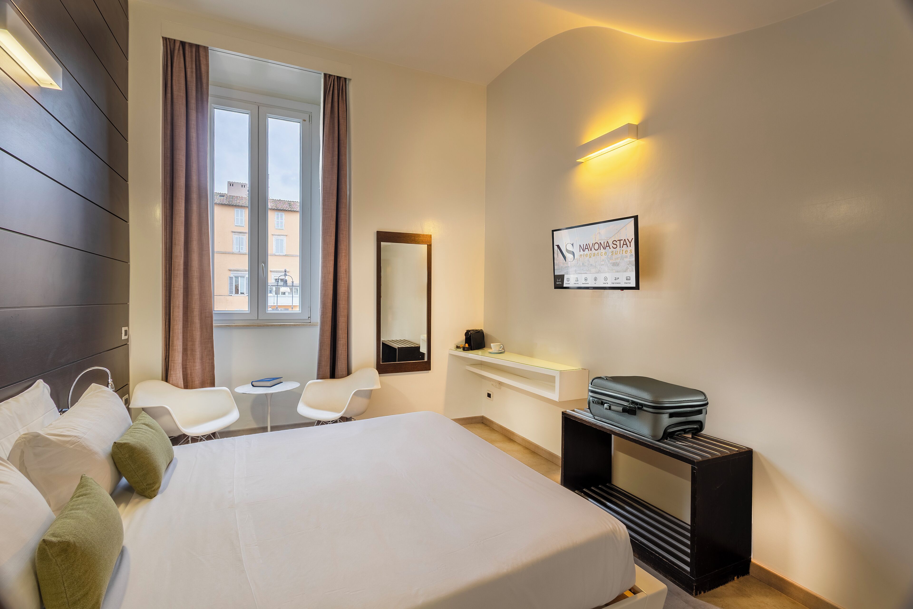 A hotel room with a bed, a desk, a chair, a mirror, and a window with curtains.