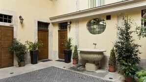 Un cortile con una fontana, piante in vaso e pavimento in pietra.
