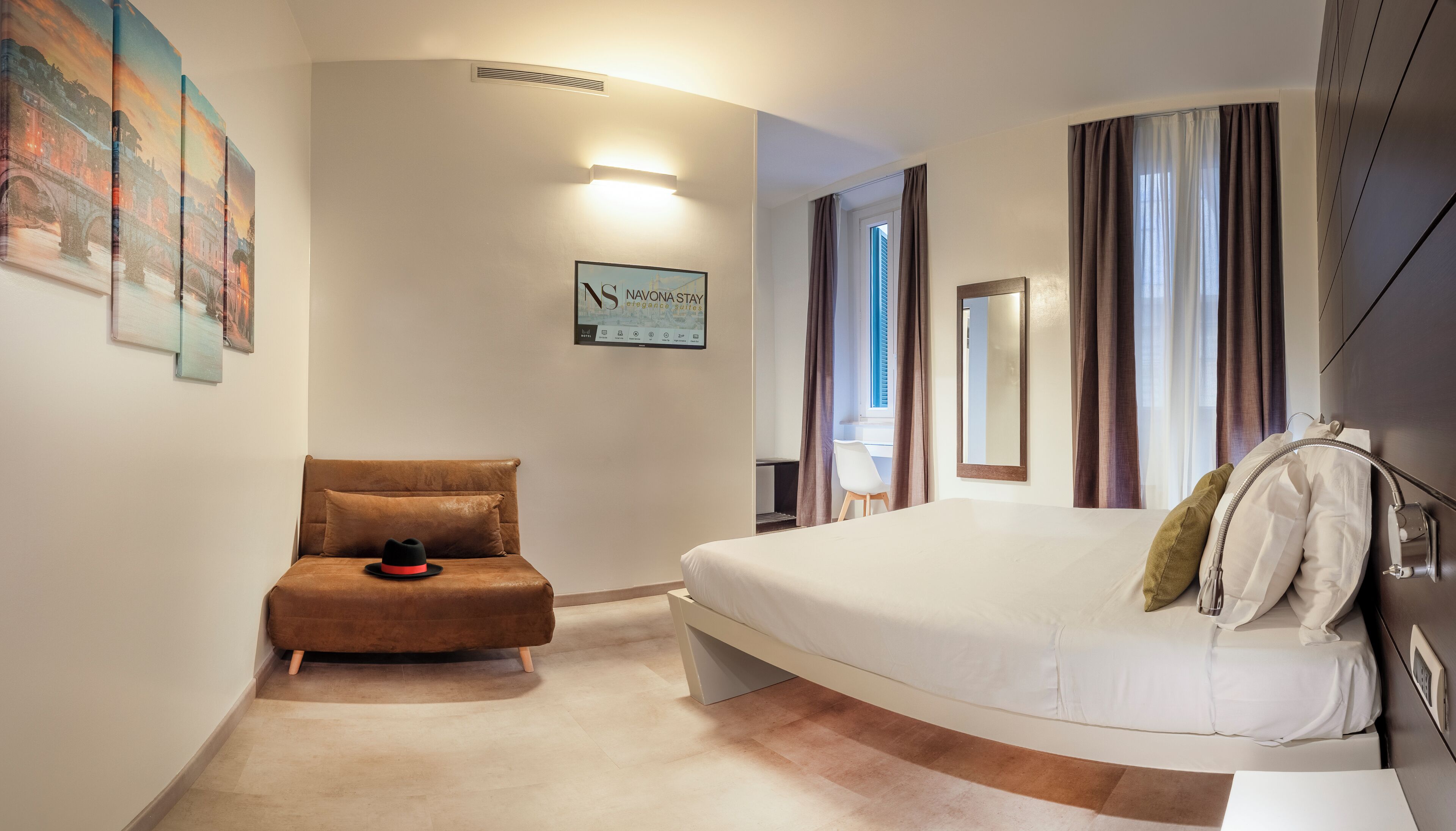 A hotel room with a bed, a chair, a desk, and a large window with curtains.