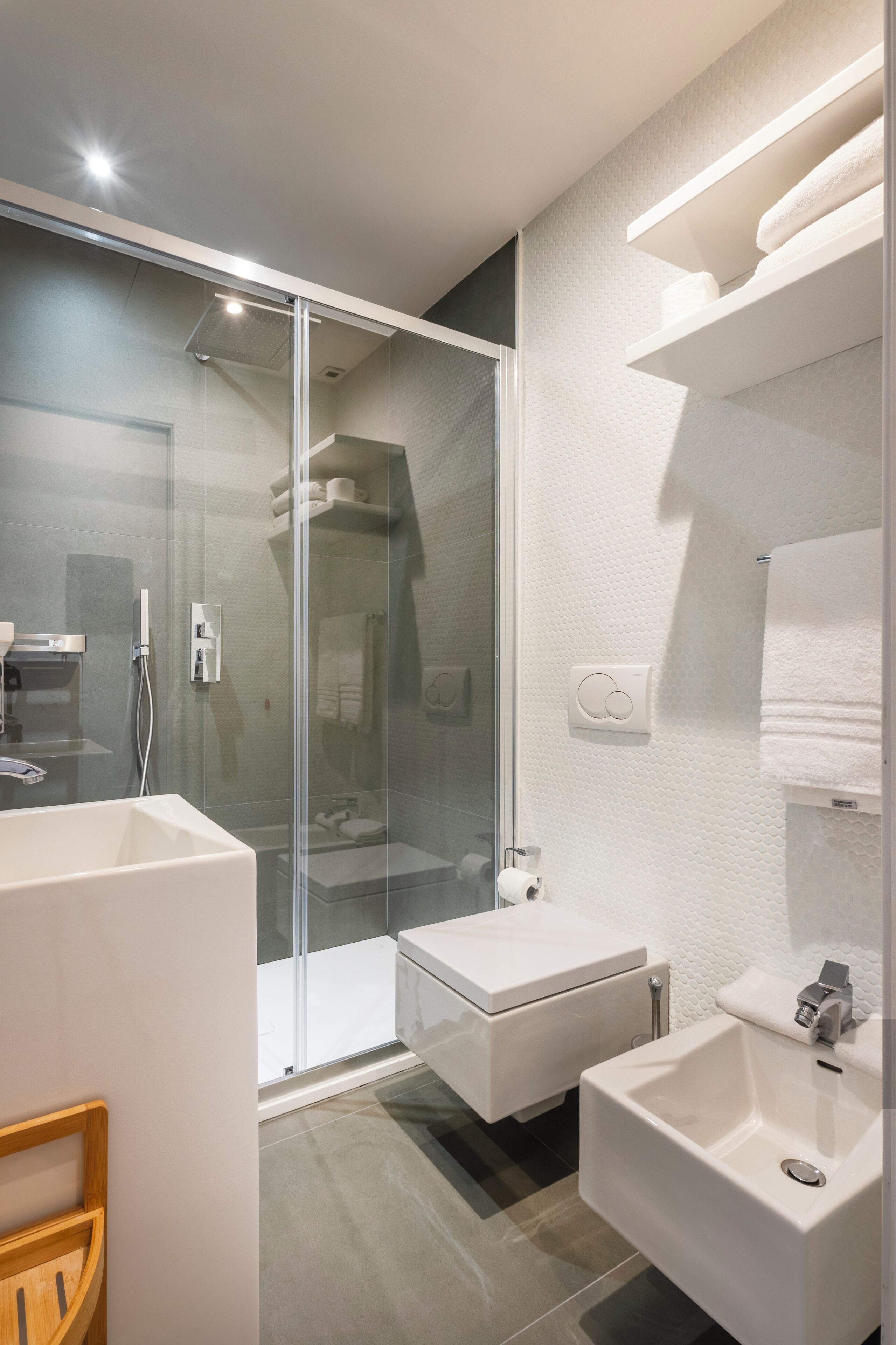 A modern bathroom with a glass-enclosed shower, a white sink, and a wooden chair.