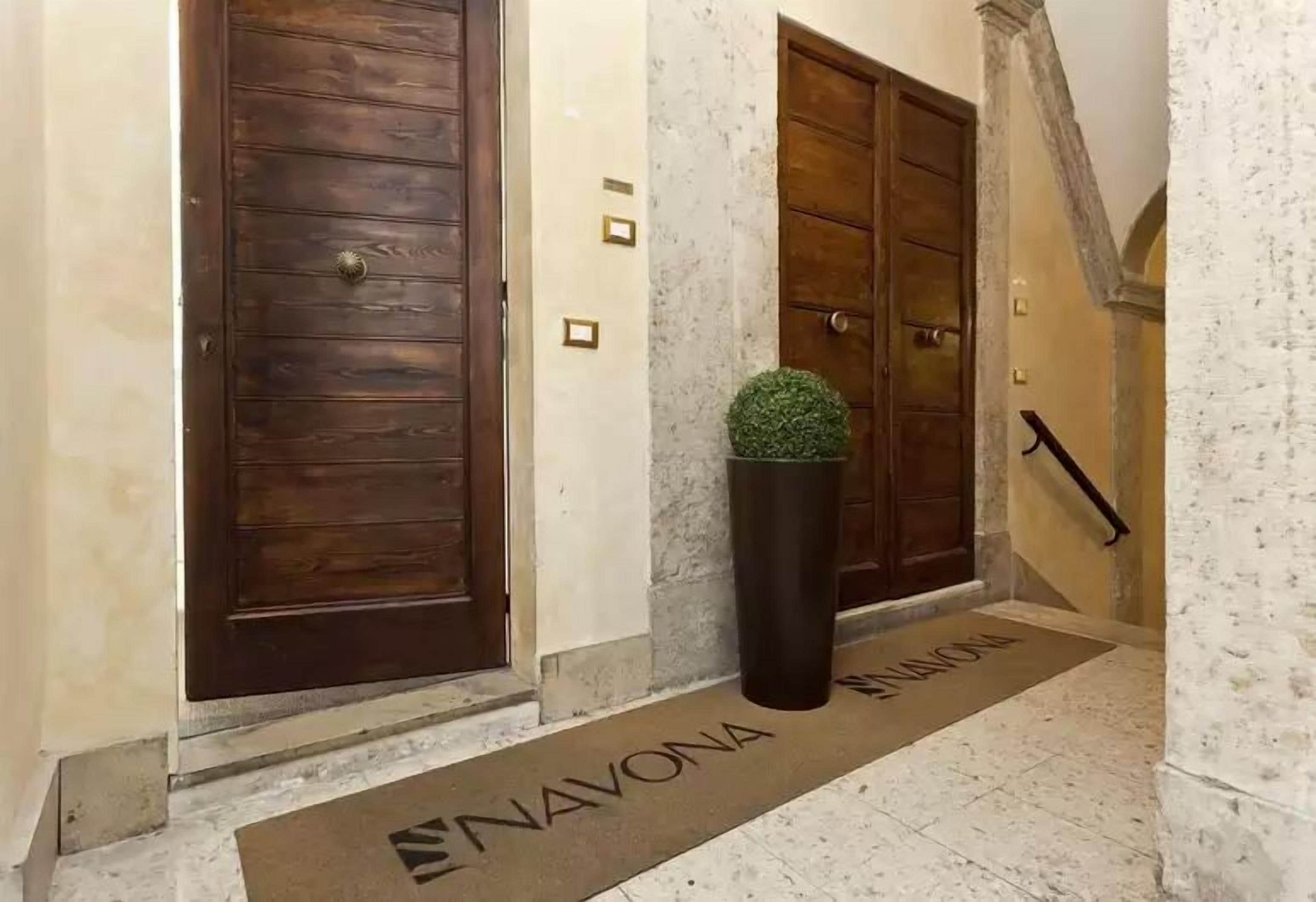A hallway with two wooden doors, a potted plant, and a doormat with the name "NAVONA".