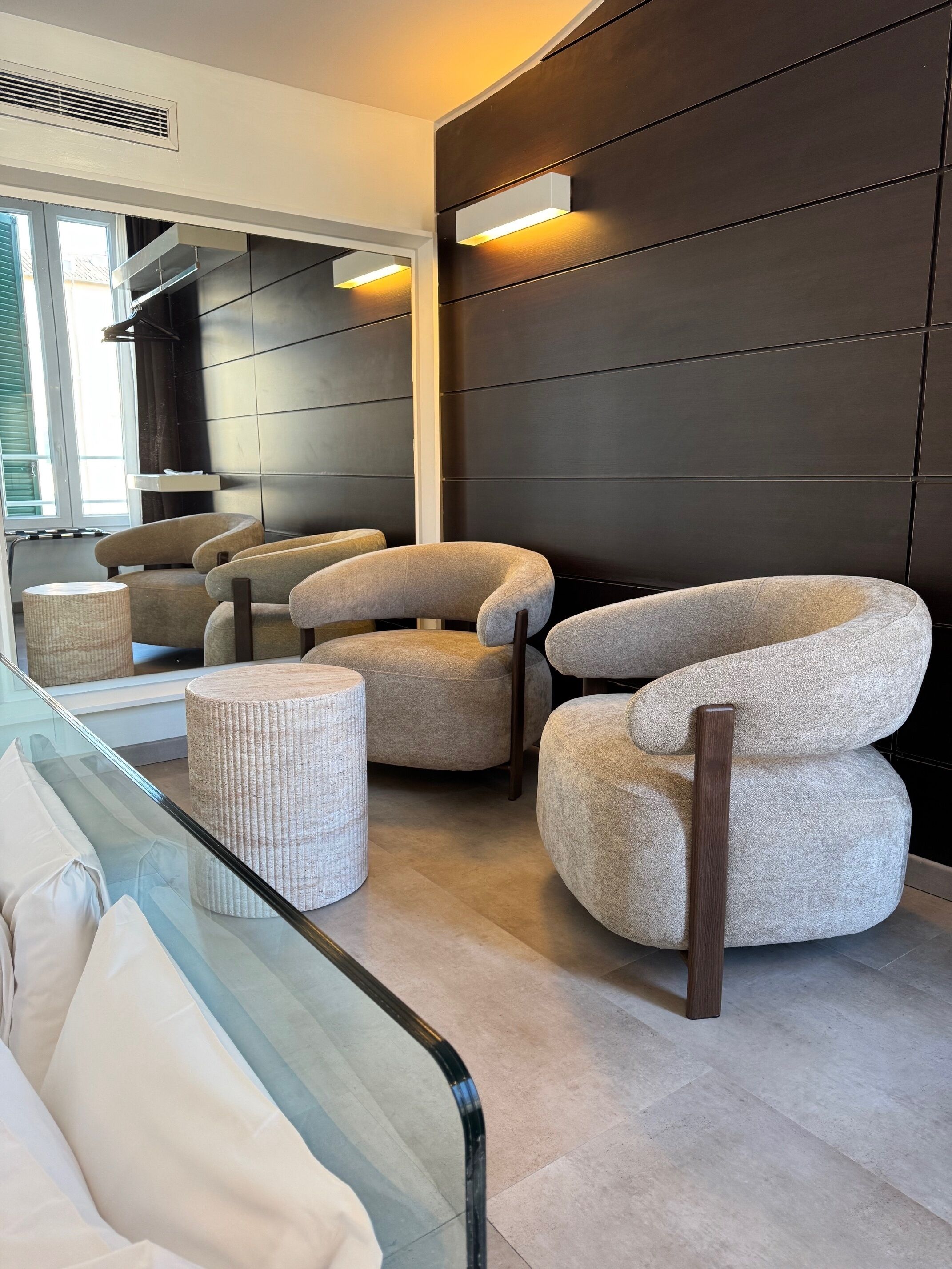 Un salon moderne avec une table basse en verre, deux fauteuils et un pouf rond.