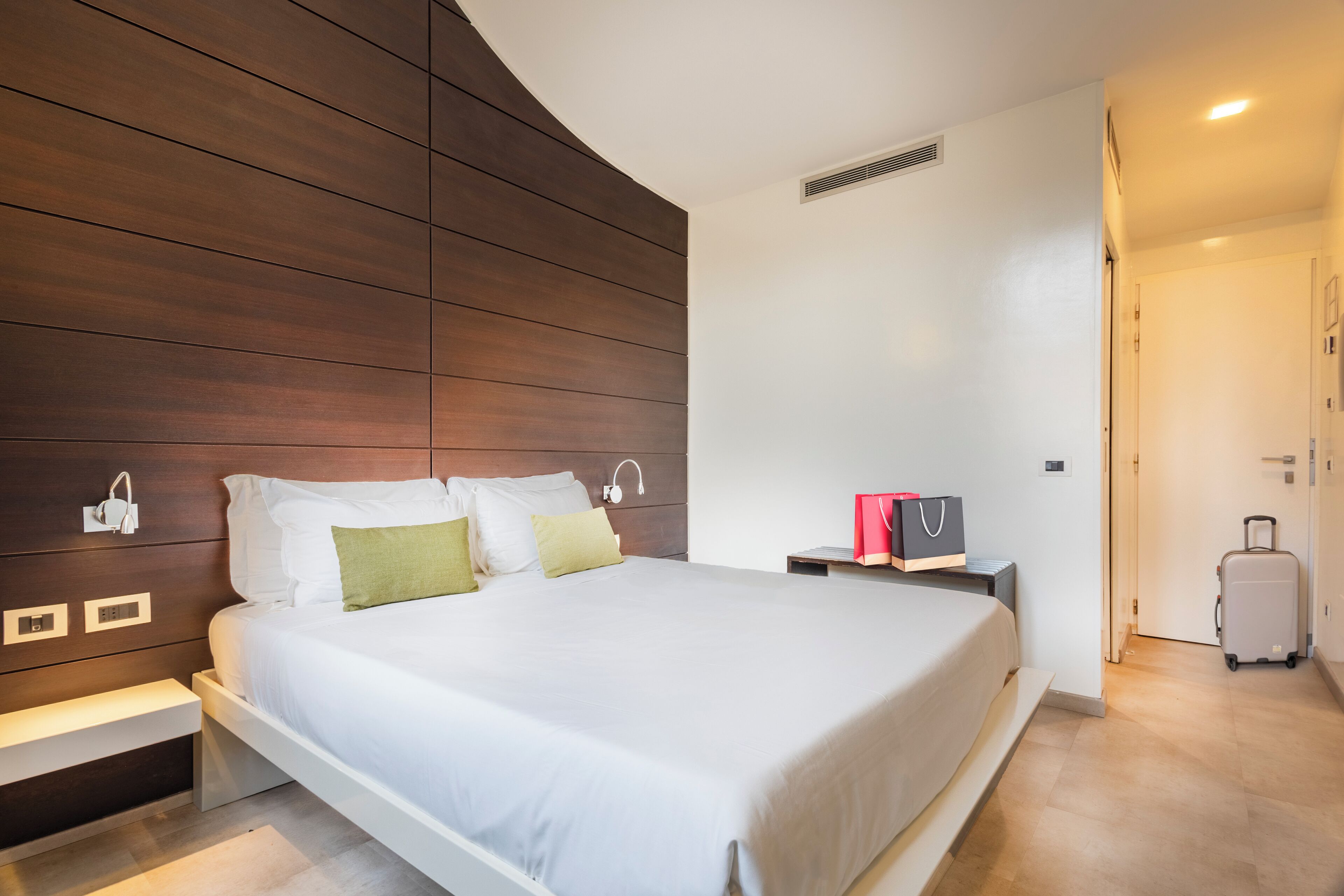 Una habitación de hotel moderna con una cama grande, una mesita de noche, un armario y una maleta.