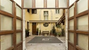 Un cortile con una fontana al centro, circondato da piante in vaso e un pavimento piastrellato.