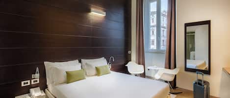 Una habitación de hotel moderna con una cama grande, una mesita de noche con teléfono, un escritorio pequeño y una silla.